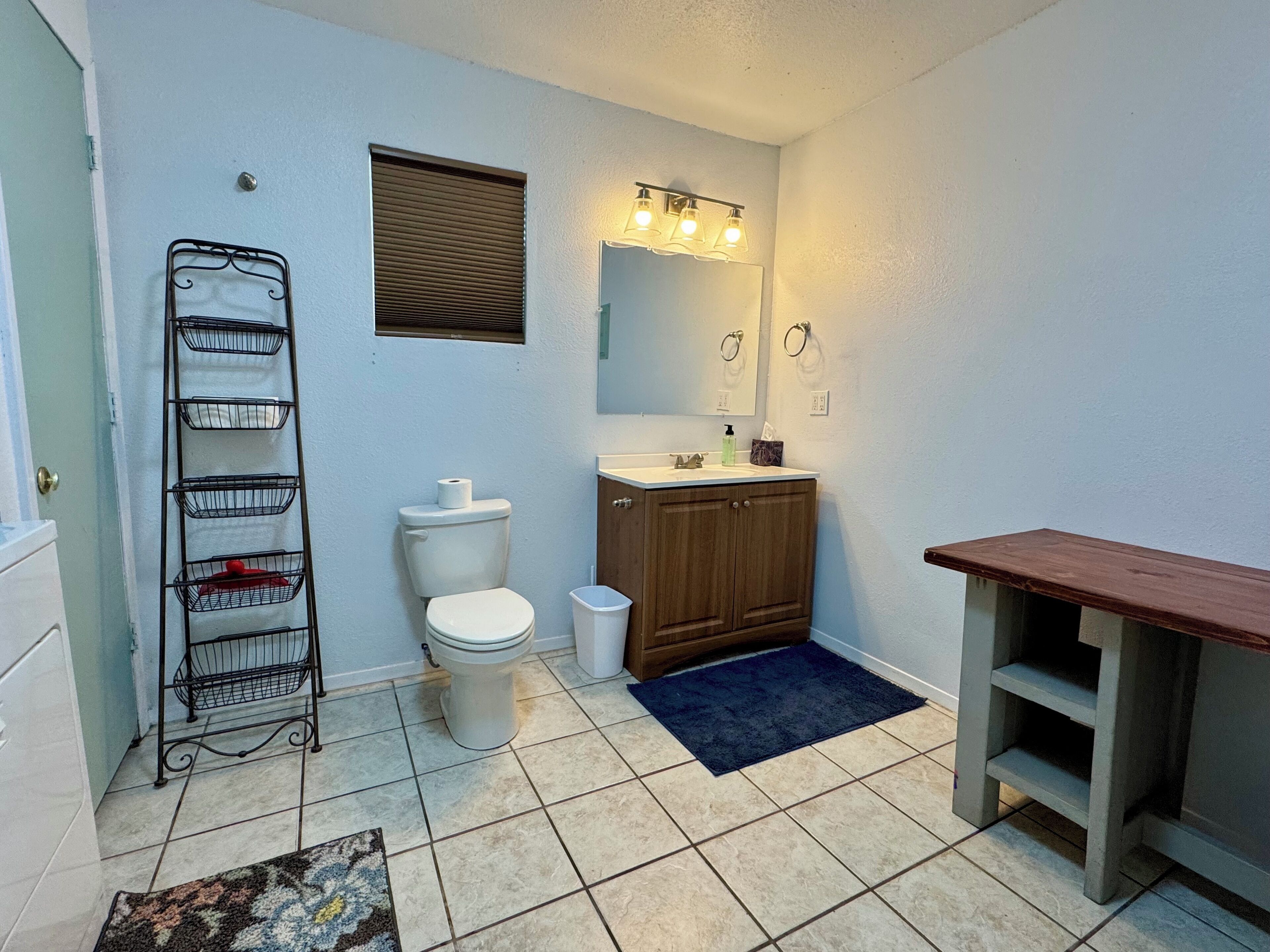 A bathroom with a toilet, sink, vanity, and a metal rack with baskets.
