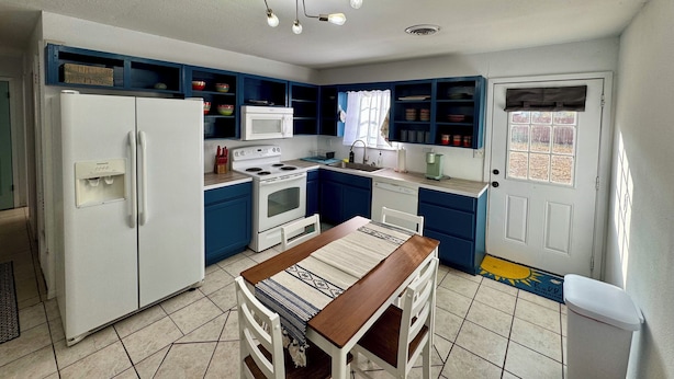 A compact kitchen with white appliances, blue cabinets, and a dining area with a wooden table and chairs.