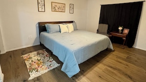 A bedroom with a bed, a ceiling fan, a floral rug, and a small table with a vase.