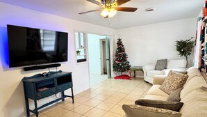 A living room with a flat-screen TV, a ceiling fan, a Christmas tree, and a sofa.