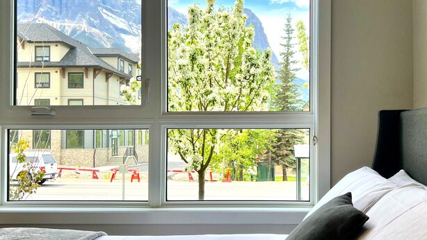 A hotel room with a large window offering views of a mountain and a tree-lined street.