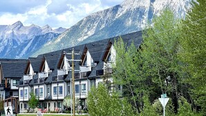 A row of chalet-style buildings with steep roofs, set against a backdrop of snow-capped mountains.