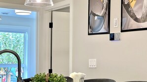 A modern dining area with a view of the outdoors, a wicker basket with greenery, a white vase, and a digital thermostat.