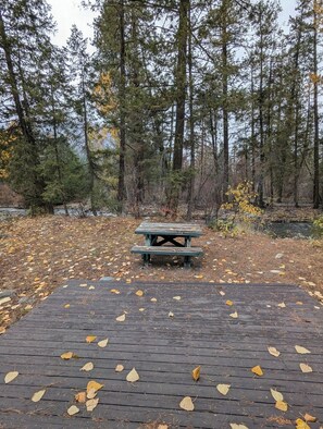 A wooden deck with a picnic table surrounded by trees and fallen leaves.