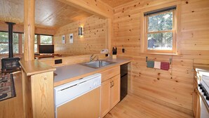 A wooden cabin interior with a kitchen area, including a sink, stove, and a window with a view of trees. - Rustic One Bedroom Cabin (Mazama)