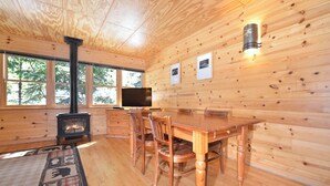 A wooden cabin interior with a fireplace, dining table, chairs, and a TV. - Rustic One Bedroom Cabin (Mazama)