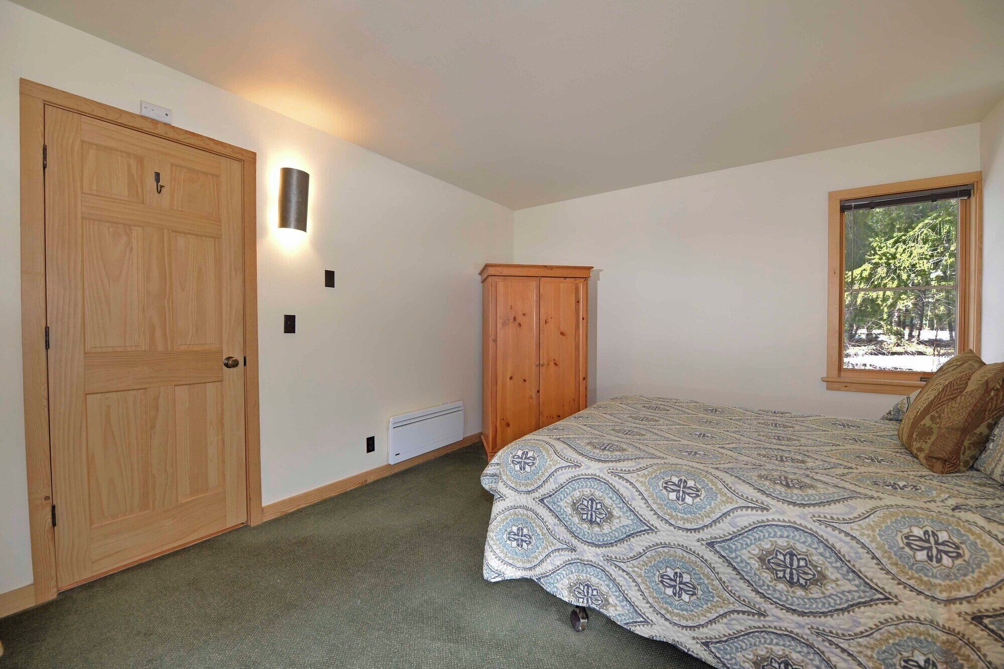 A bedroom with a bed, a wardrobe, a heater, and a window with a view of trees.