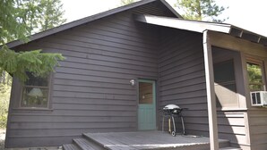 A cabin with a front porch, a door, and a grill. - Rustic One Bedroom Cabin (Mazama)