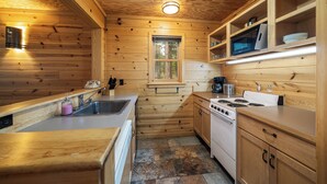 A compact kitchen with wooden walls, a window, a sink, a stove, and a microwave.