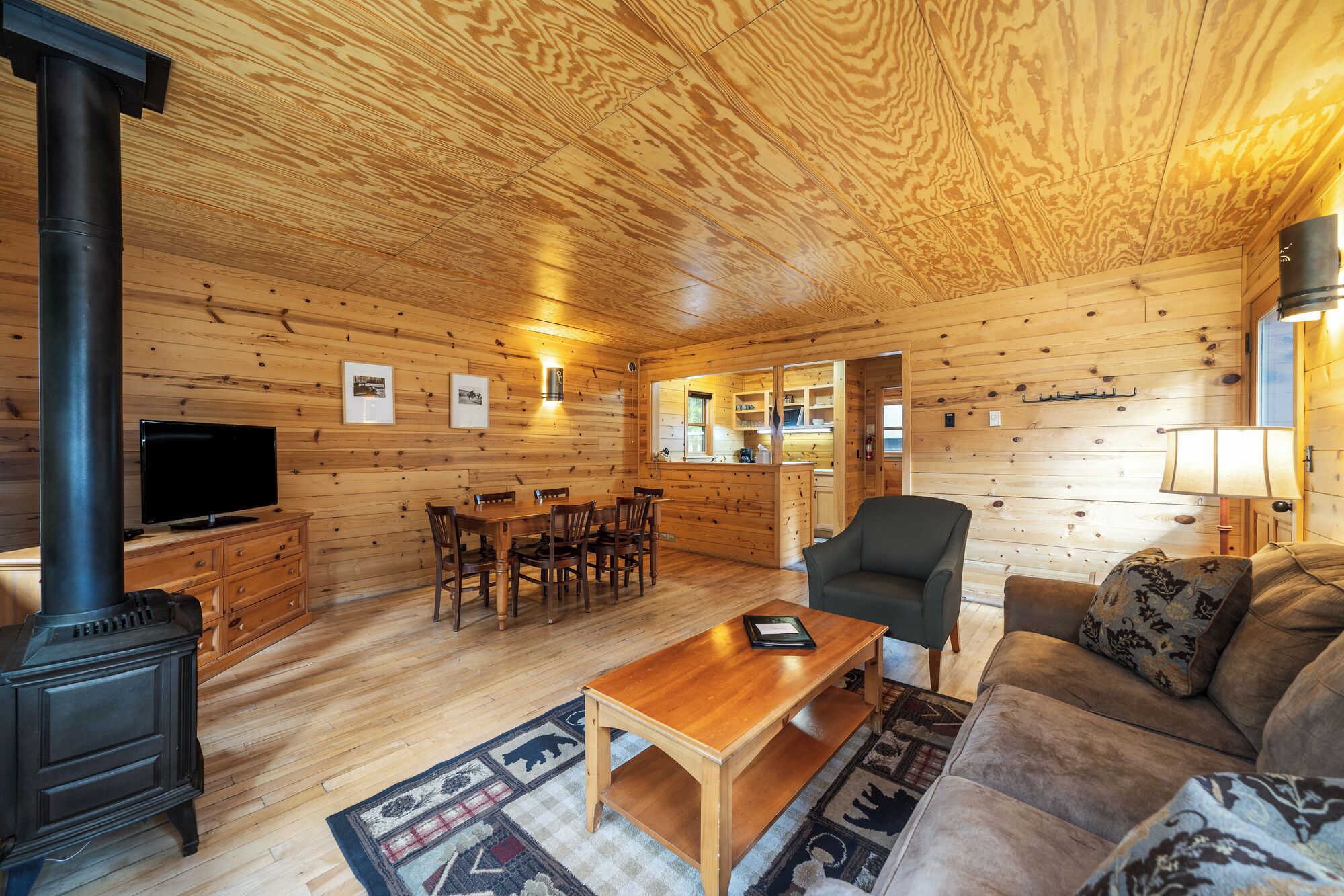 En mysig stuga med en matplats, en soffa, en tv och en vedkamin.