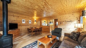 A cozy cabin interior with a dining area, a sofa, a TV, and a wood stove.