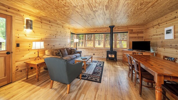 A cozy cabin interior with a sofa, TV, dining table, and a fireplace.
