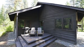 A cabin with a porch, a grill, and two Adirondack chairs.