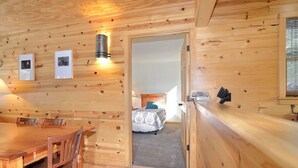 A wooden interior with a dining area, a bed with a patterned bedspread, and a hallway leading to another room.