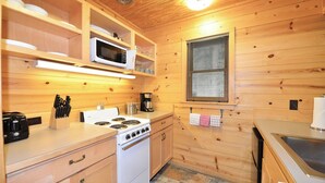 A compact kitchen with wooden walls, a stove, a microwave, and a sink. - Rustic Two Bedroom Cabin (Mazama)