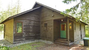A rustic cabin with a green door, a porch, and a small window. - Rustic Two Bedroom Cabin (Mazama)