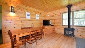 A wooden cabin interior with a dining table, chairs, a television, and a wood-burning stove. - Rustic Two Bedroom Cabin (Mazama)