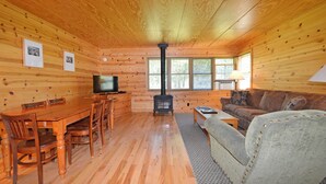 A cozy cabin interior with a wooden interior, a dining area with a table and chairs, a sofa, a television, and a fireplace. - Rustic Two Bedroom Cabin (Mazama)