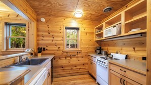 A wooden cabin kitchen with a sink, stove, microwave, and cabinets.