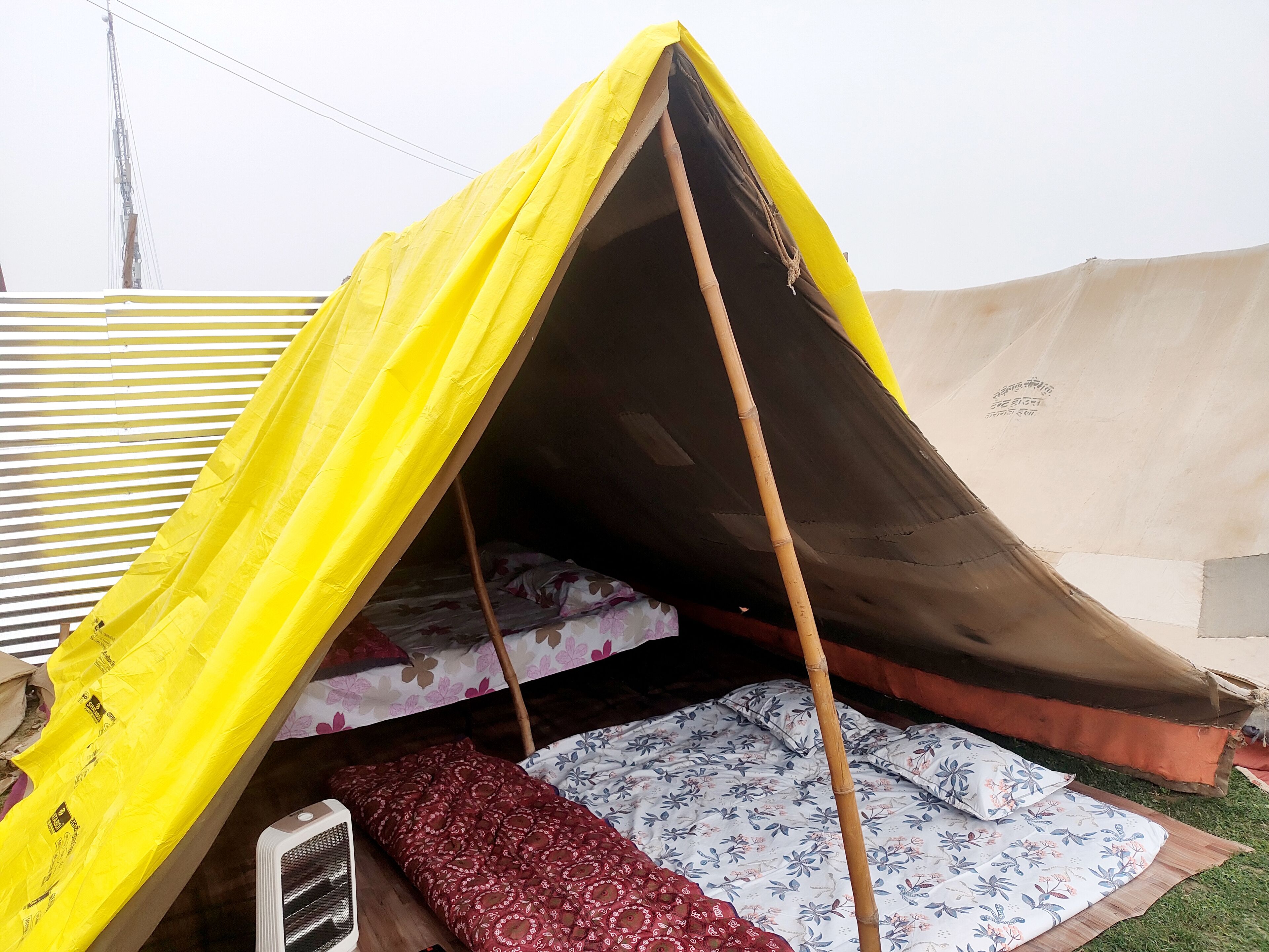 Una carpa con dosel amarillo y marrón, un poste de bambú y un colchón con ropa de cama estampada de flores.