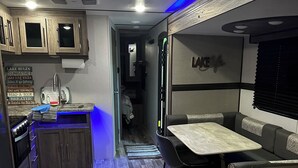 Un intérieur de camping-car compact comprenant un coin cuisine, un espace repas et un espace nuit.