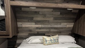 Une chambre avec un plafond en lambris de bois, un lit avec du linge de lit blanc, une couverture à rayures et un oreiller orné d’un motif textuel.