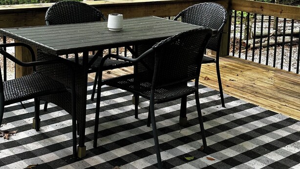 Une terrasse extérieure en bois, dotée d’un sol à carreaux, entourée d’arbres.