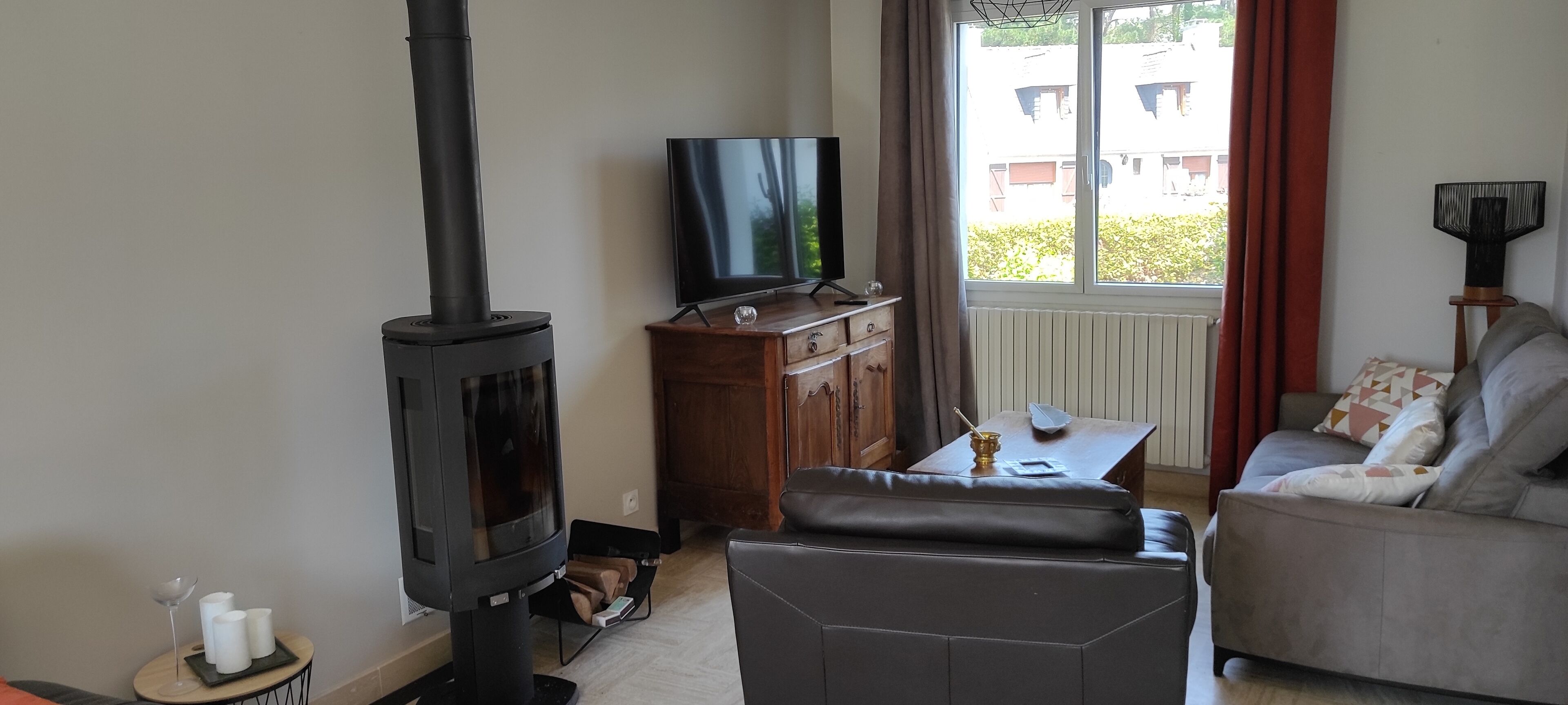 Ein Wohnzimmer mit einem schwarzen Kaminofen, einem Fernseher auf einem Holzschrank, einem Sofa und einem Fenster mit Vorhängen.