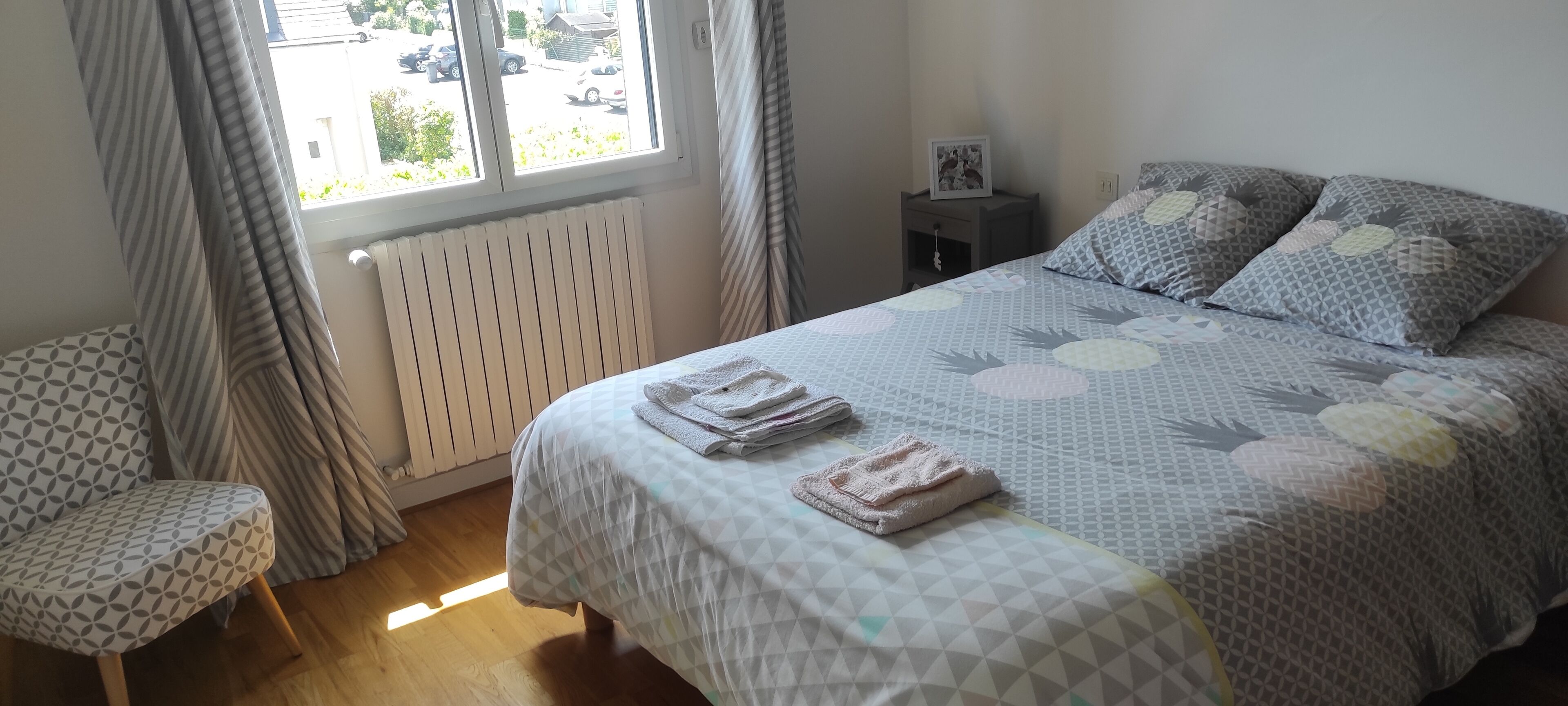 A bedroom with a bed, a chair, a nightstand, and a window with curtains.