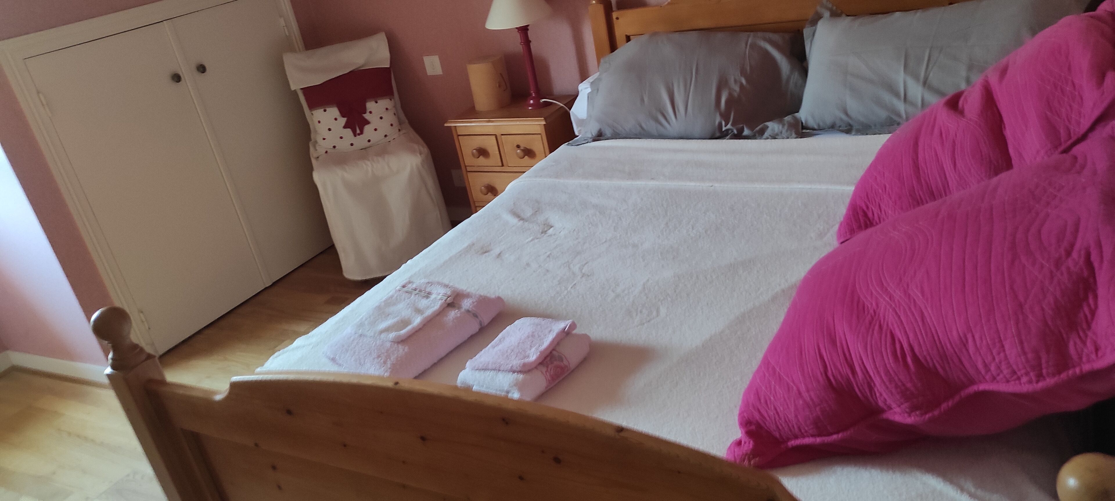 A bedroom with a bed, pillows, a nightstand, a wardrobe, and a pair of towels.