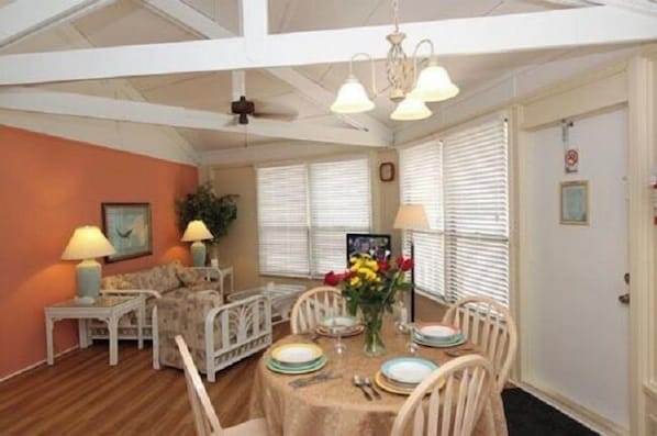 A dining area with a table set for four, surrounded by white chairs, a sofa, and a small side table with a lamp. - The Reef at Marathon, Florida Keys (Marathon)