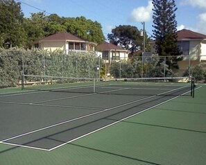 Ulkotenniskenttä, jossa on verkko, ja jonka ympärillä on aita ja puita.