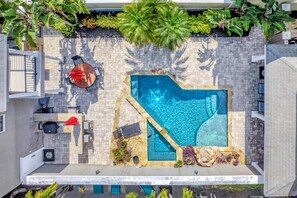 Una piscina en la azotea con una forma singular, rodeada por un patio con baldosas y abundante vegetación.