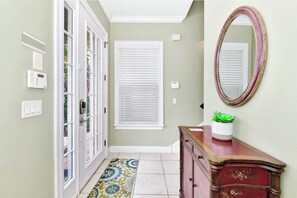 A hallway with a door, a window with blinds, a mirror, a cabinet, and a patterned rug.