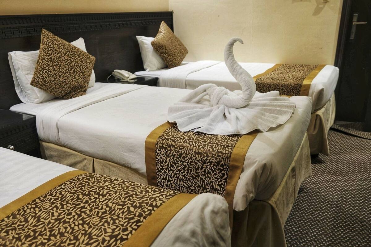 Une chambre d’hôtel avec deux lits, chacun recouvert d’une couvre-lit à motifs et agrémenté d’oreillers. Une serviette en forme de cygne est posée sur le lit, au premier plan.