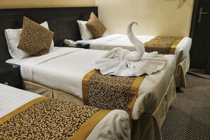 A hotel room with two beds, each with a patterned bedspread and pillows. A swan-shaped towel is placed on the bed in the foreground.