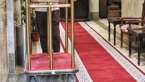 Ein Mann schiebt einen goldenen Gepäckwagen in eine Lobby mit Marmorwänden, einem roten Teppich und Möbeln.