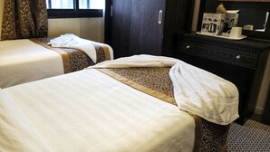Ein Hotelzimmer mit zwei Betten, einer dunklen Holzkommode und einem Fenster mit Vorhängen.