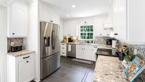 A modern kitchen with white cabinetry, stainless steel appliances, granite countertops, and a large window providing natural light. - Luxury Retreat & Heated Pool Downtown Simpsonville (Simpsonville)