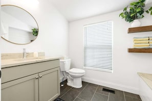 A bathroom with a toilet, sink, mirror, and window with blinds.