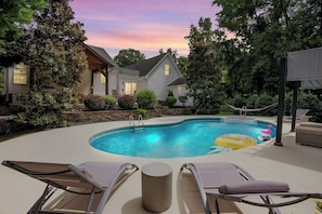 A backyard with a swimming pool, lounge chairs, and a house.
