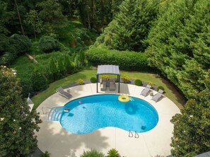 A circular pool with lounge chairs and a canopy, surrounded by lush greenery.