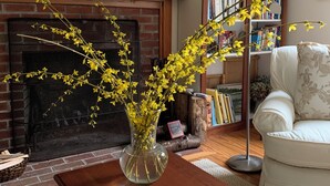 A living room with a fireplace, a bookshelf, a white armchair, and a vase with yellow flowers on a wooden table. - Beautiful Nantucket summer escape,  3 bed house, quiet office, central location  (Nantucket)