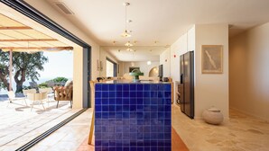 A modern kitchen with a blue tile island, a refrigerator, and a dining area with chairs. - 180° sea view villa, renovated in 2024, a little paradise in Rayol Canadel (Rayol-Canadel-sur-Mer)