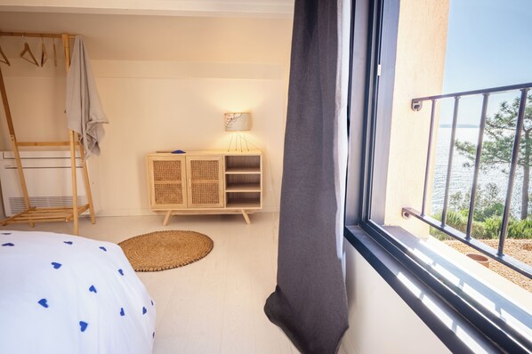 Un dormitorio con cama, armario de madera, mesita de noche con lámpara y vista al mar desde un balcón.