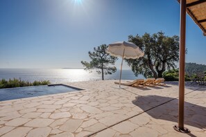 A stone patio with a pool, lounge chairs, and an umbrella. - 180° sea view villa, renovated in 2024, a little paradise in Rayol Canadel (Rayol-Canadel-sur-Mer)