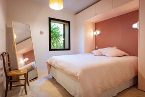 A bedroom with a bed, a chair, a mirror, and a window with a view of trees. - 180° sea view villa, renovated in 2024, a little paradise in Rayol Canadel (Rayol-Canadel-sur-Mer)