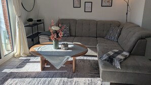Ett vardagsrum med en soffa, ett soffbord, en krukväxt och inramade tavlor på väggen.