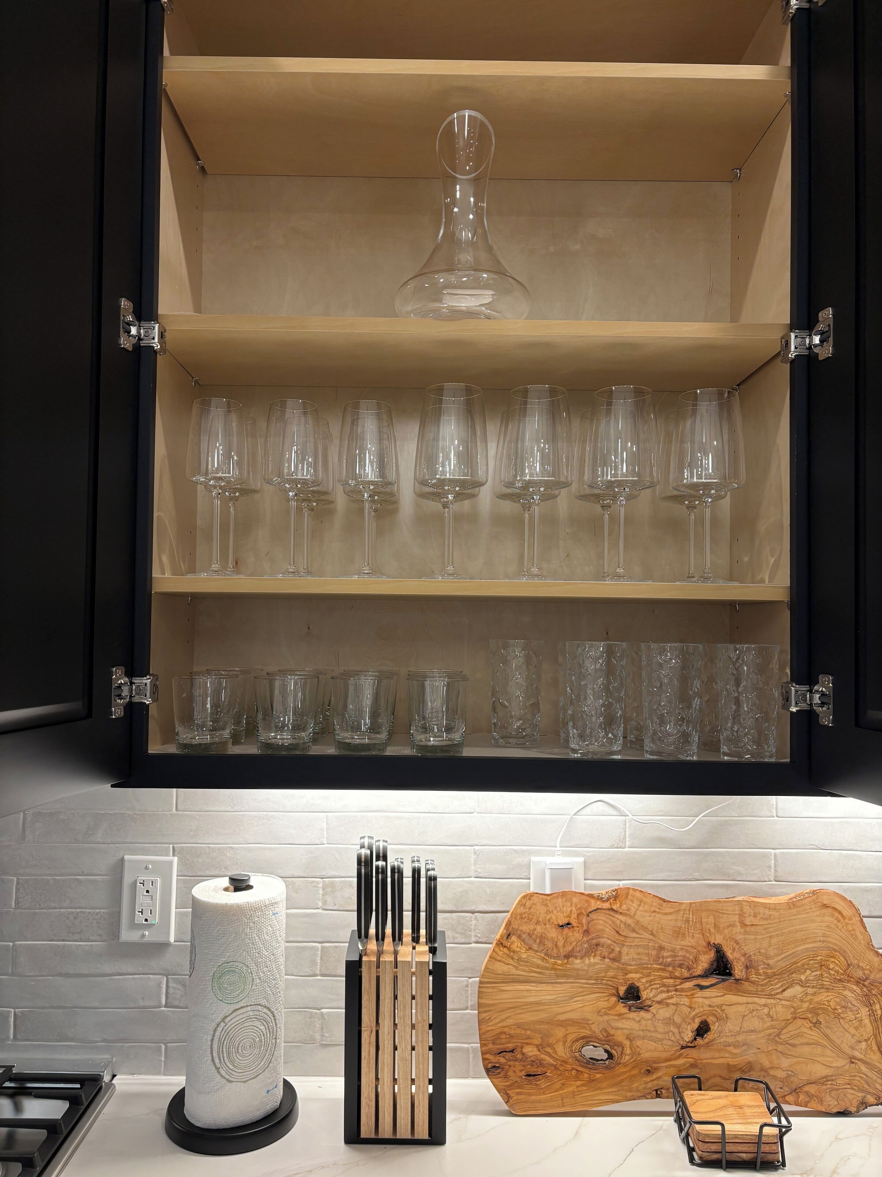 Une cuisine avec un meuble en bois contenant des verres à vin et une grande planche à découper en bois.