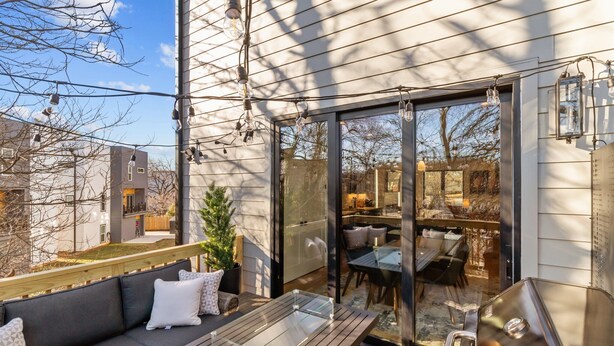Un patio exterior con terraza de madera, zona de comedor cubierta con vidrio y una parrilla.